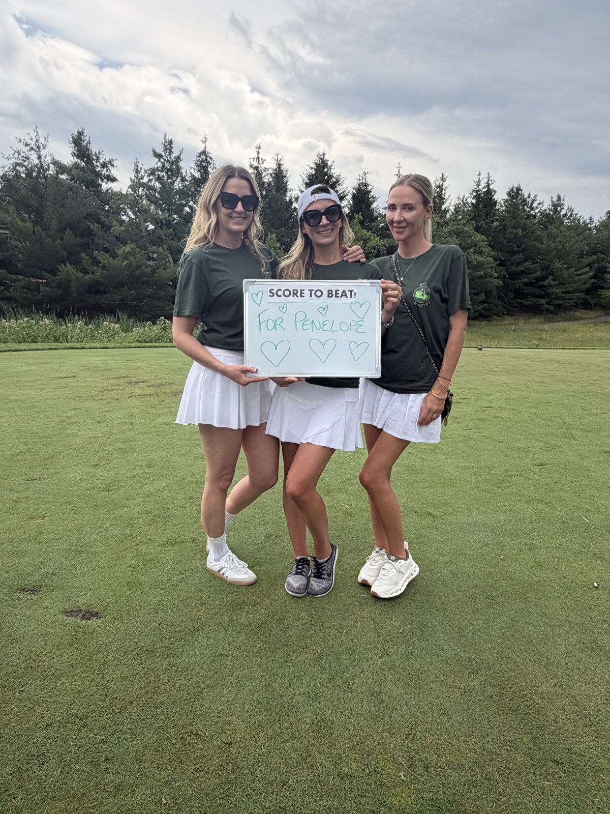 Three supporters on the green holding a sign that reads &ldquo;Score to beat: for Penelope&rdquo;